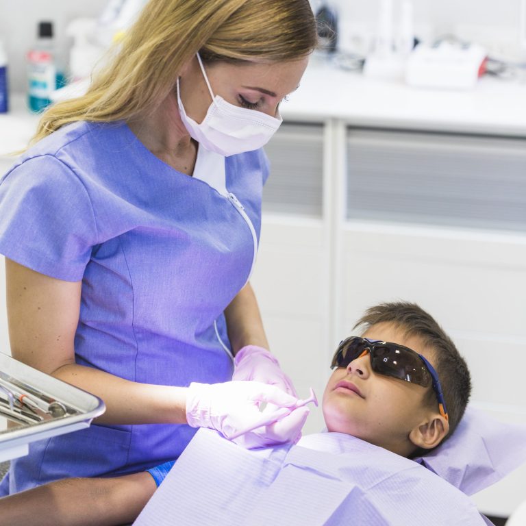female-dentist-checking-boy-s-teeth-with-dental-mirror